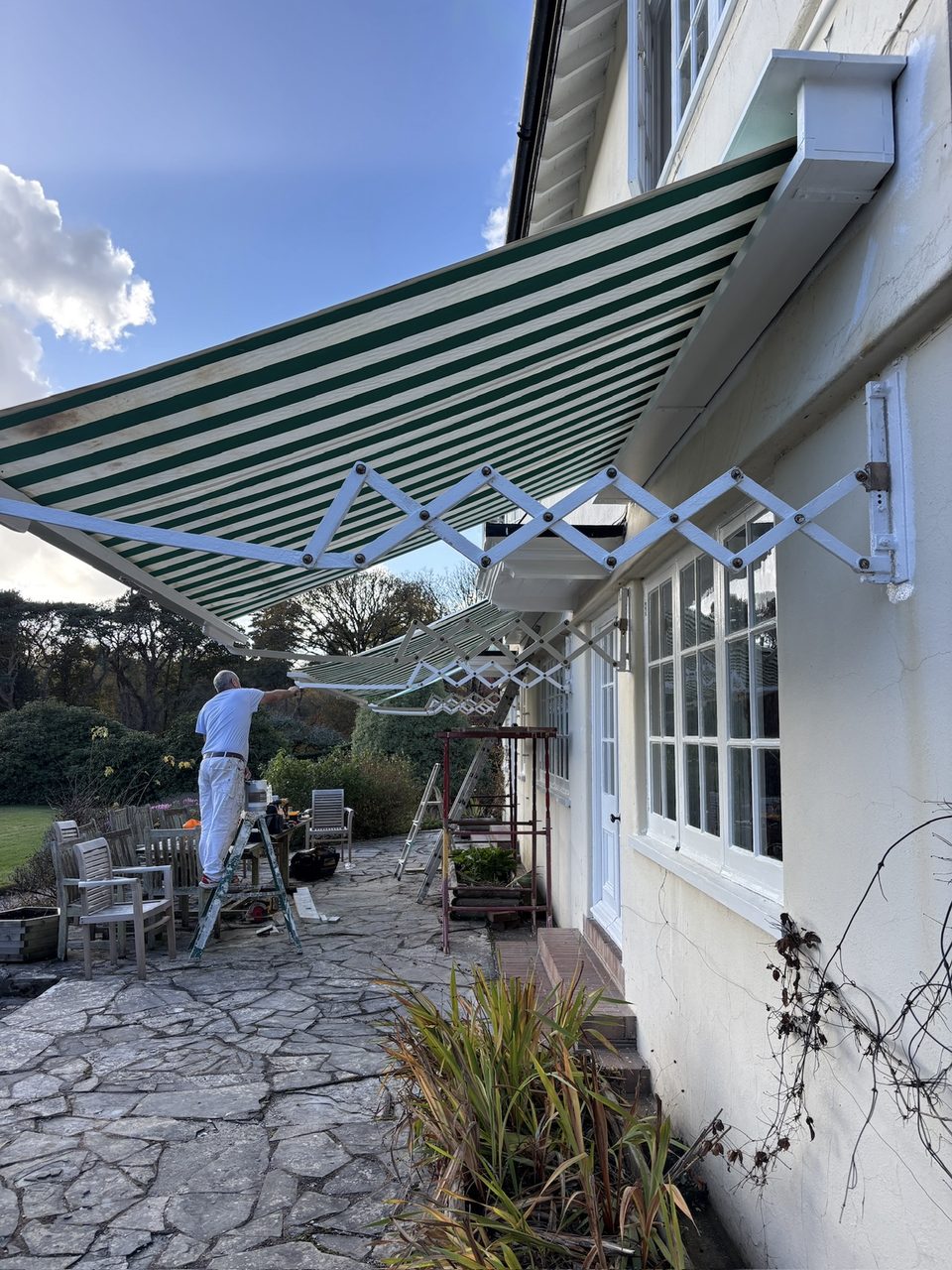 Retractable awning with white folding arms on the side of a house