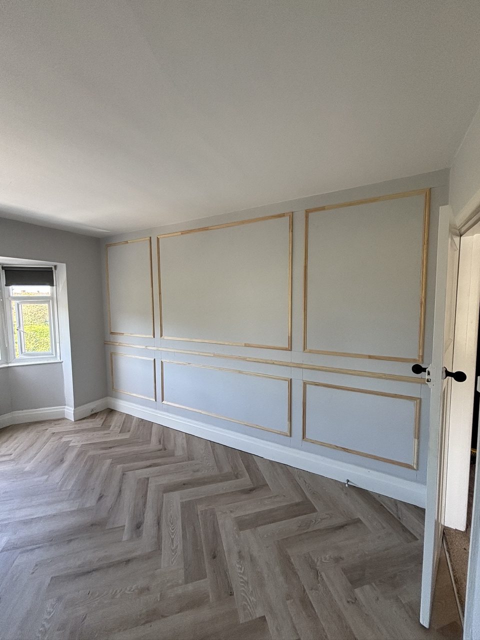 Fitted wall panel mouldings above a herringbone floor in a bedroom